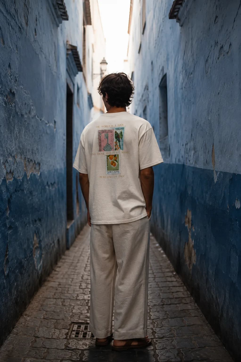 A man stands in a narrow blue-washed alley wearing the St. Augustine tee